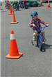 Child With Training Wheels Rides Next to Cone