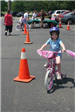 Young Girl Smiles as She Drives Bike Next to Cone