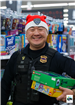 An officer is shown smiling holding gifts under his arm