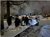 A diverse group of adults working together, behind folding tables outside in the snow