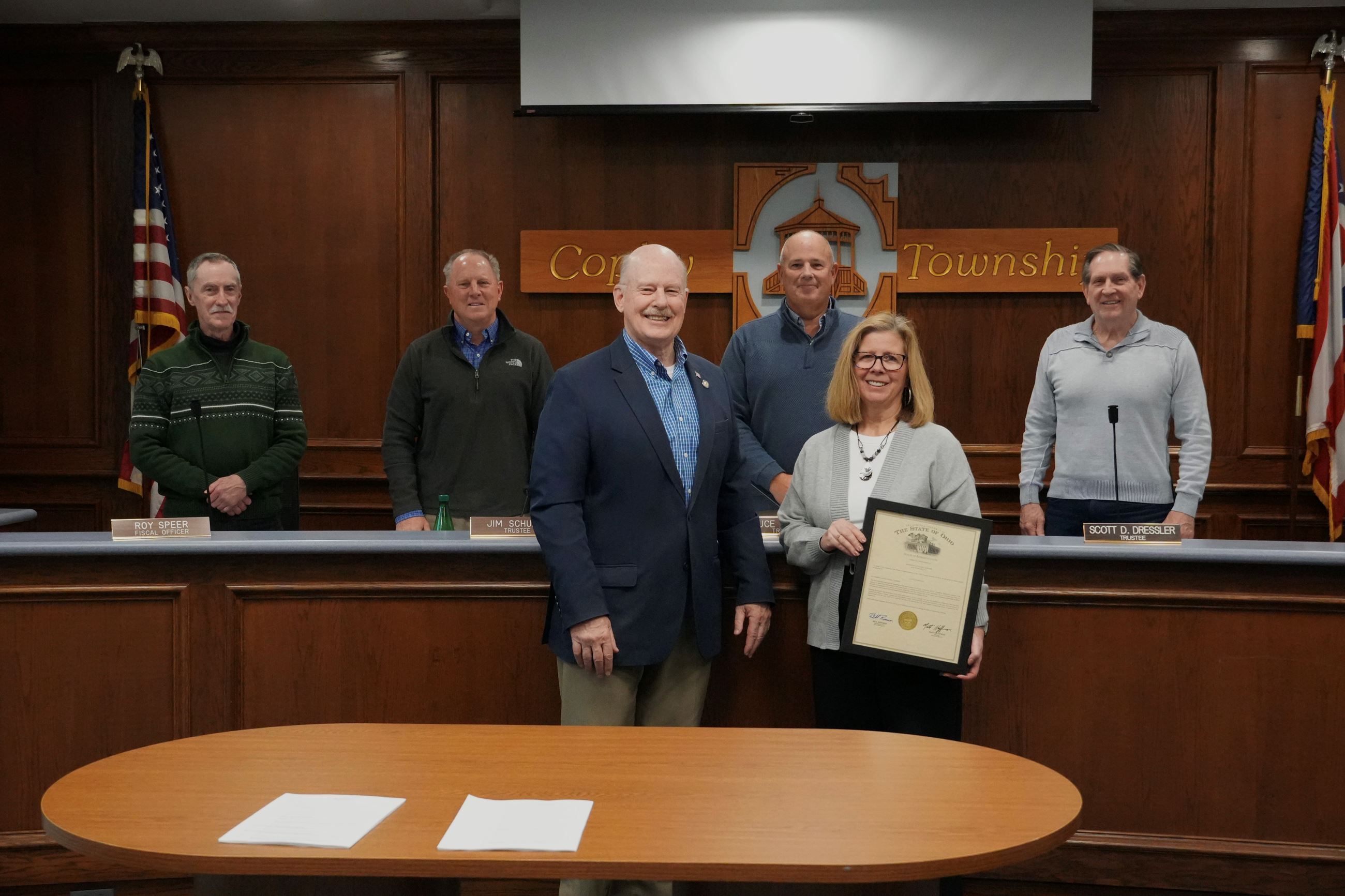 A group of people are standing together where a man is delivering a plaque to a woman