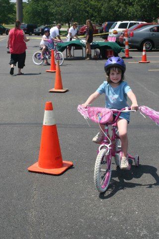 Young Girl Smiles as She Drives Bike Next to Cone