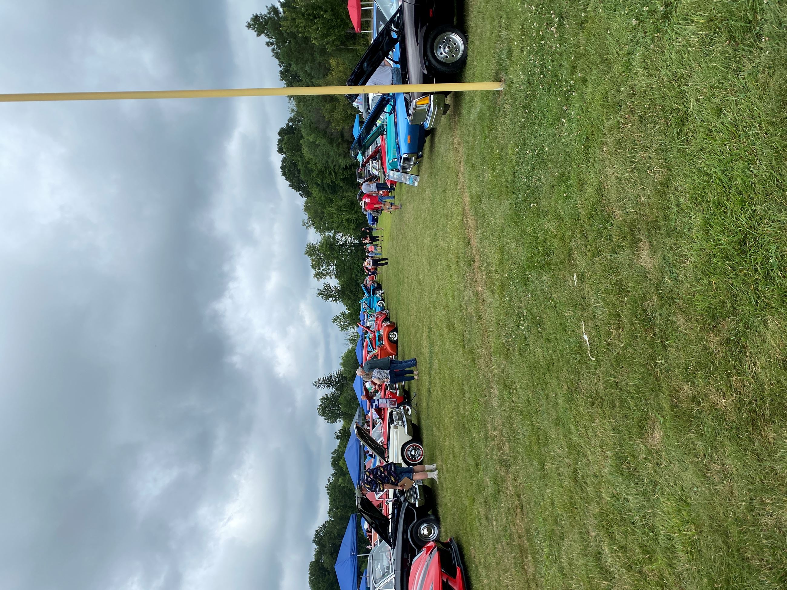 A row of cars with people lined up to view the cars and speak with the car owners