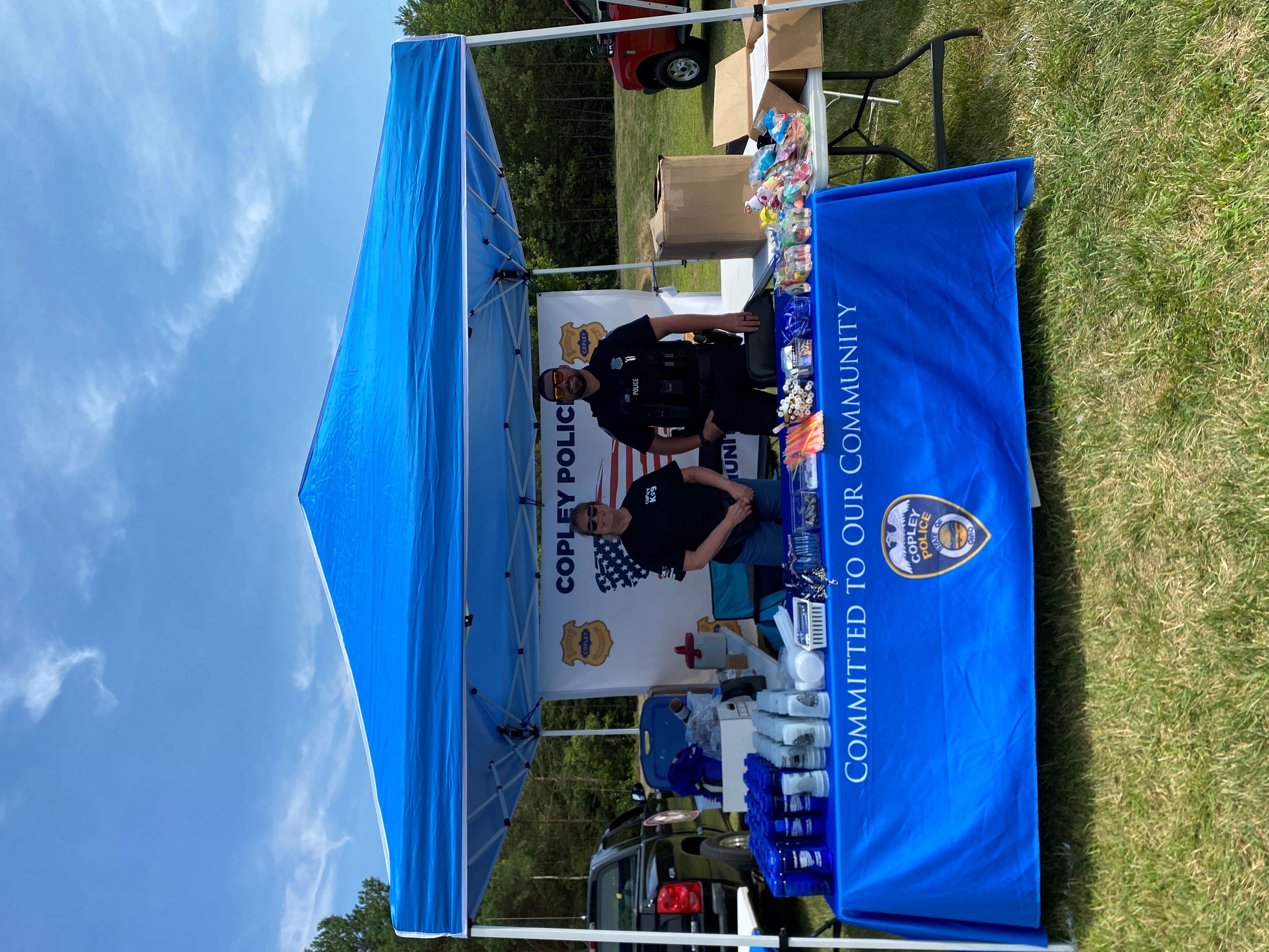 Officer Harris and Admin. Assistant Sheryl at the Copley Police Blue Tent with Blue Table Cloth Reading "Committed to our Community"