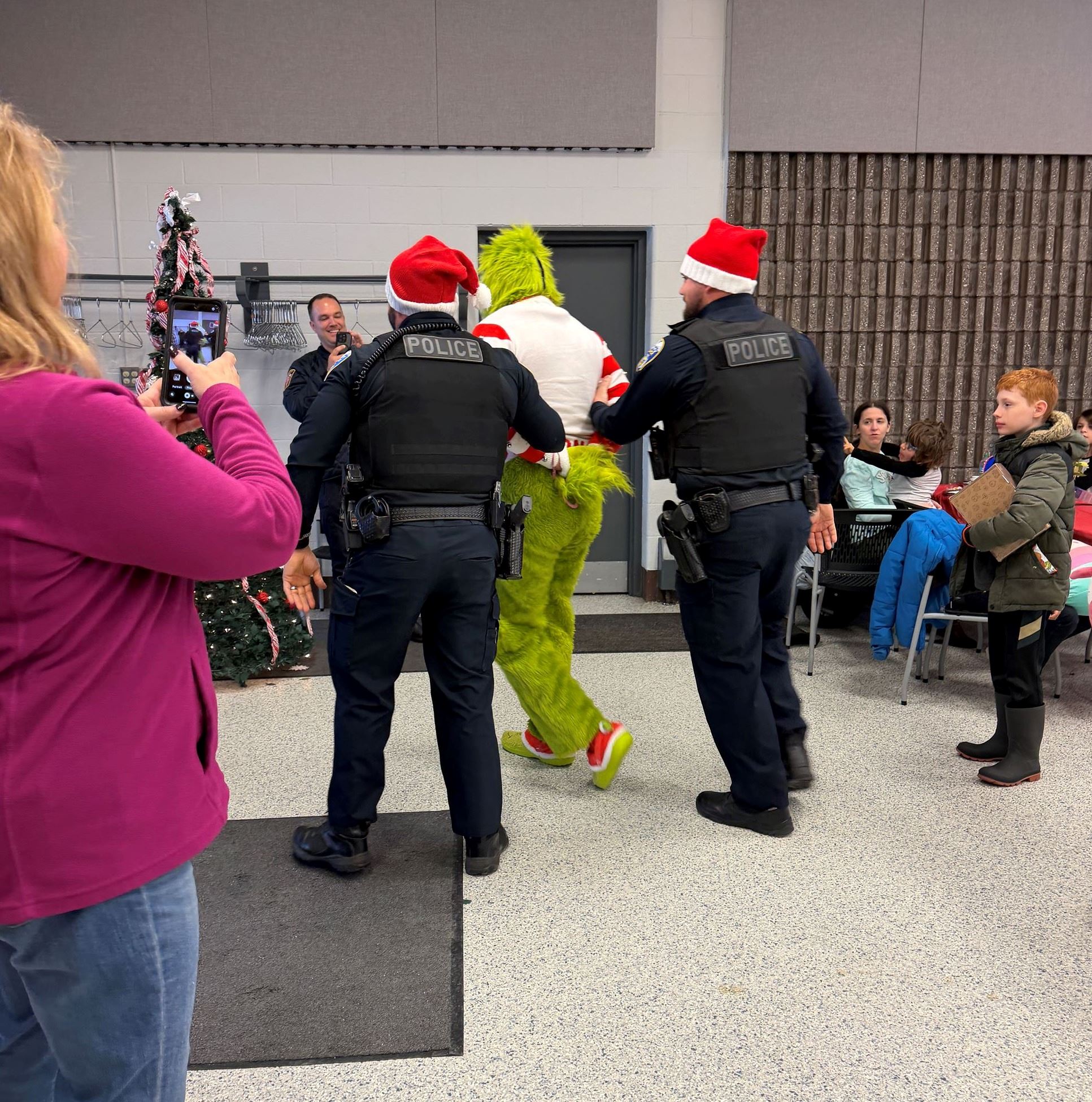 An officer stands on either side of a handcuffed Grinch