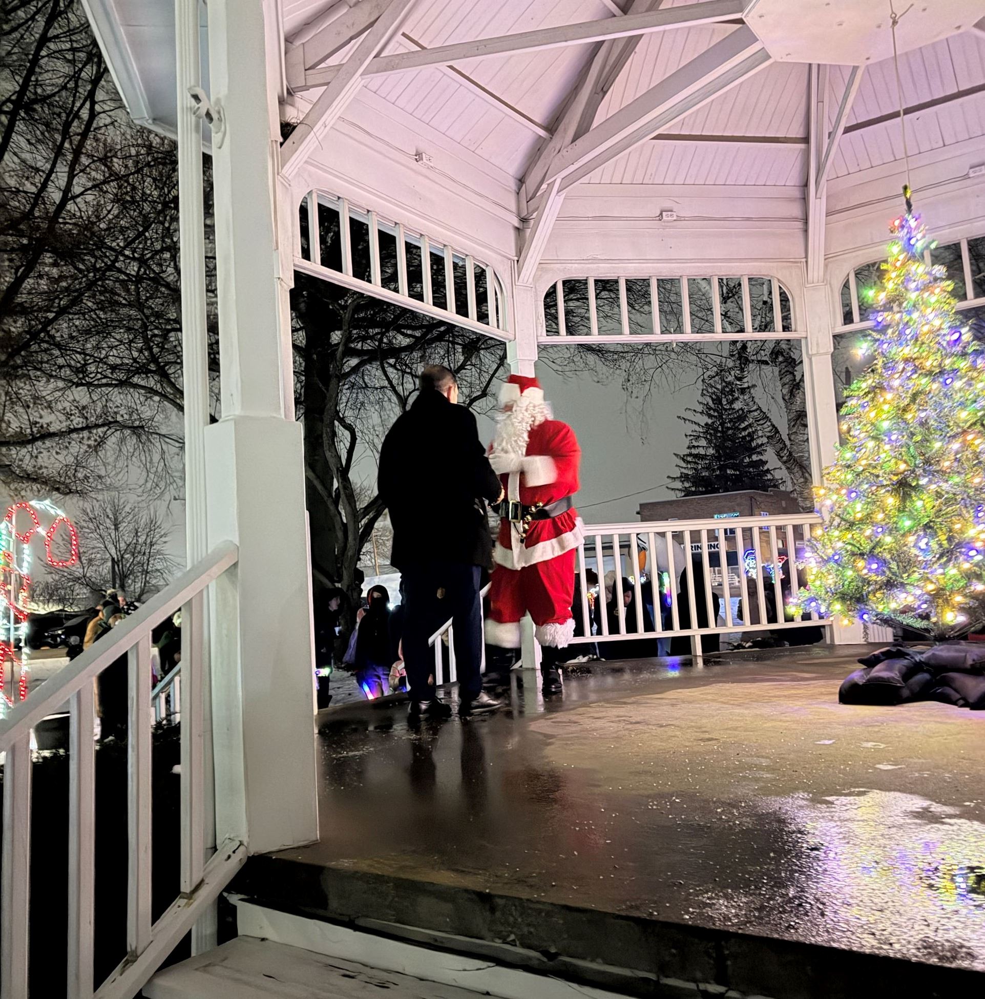 A man is seen standing on the Gazebo stage with Santa Claus and a Christmas Tree